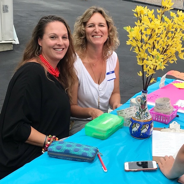 Two women, members of the PTSA of Shelter Island, sit at a table outside the school selling raffle tickets and taking reservations for an event.